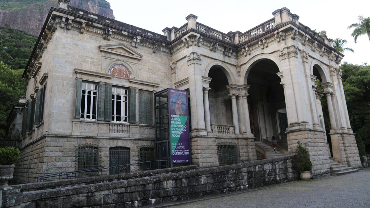 Foto da fachada da Escola de Artes Visuais do Parque Lage com o cartaz de uma mostra pendurado
