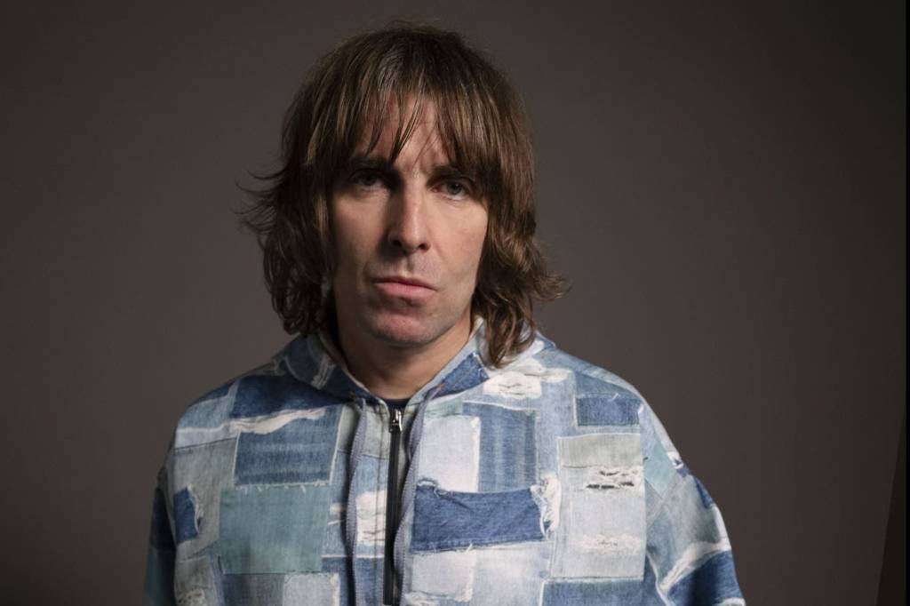 O cantor Liam Gallagher tem os cabelos lisos e castanhos claros um pouco acima da altura do ombro. Ele usa uma camisa feita com retalhos de jeans de diversas tonalidades. Está sério e olhando para a câmera