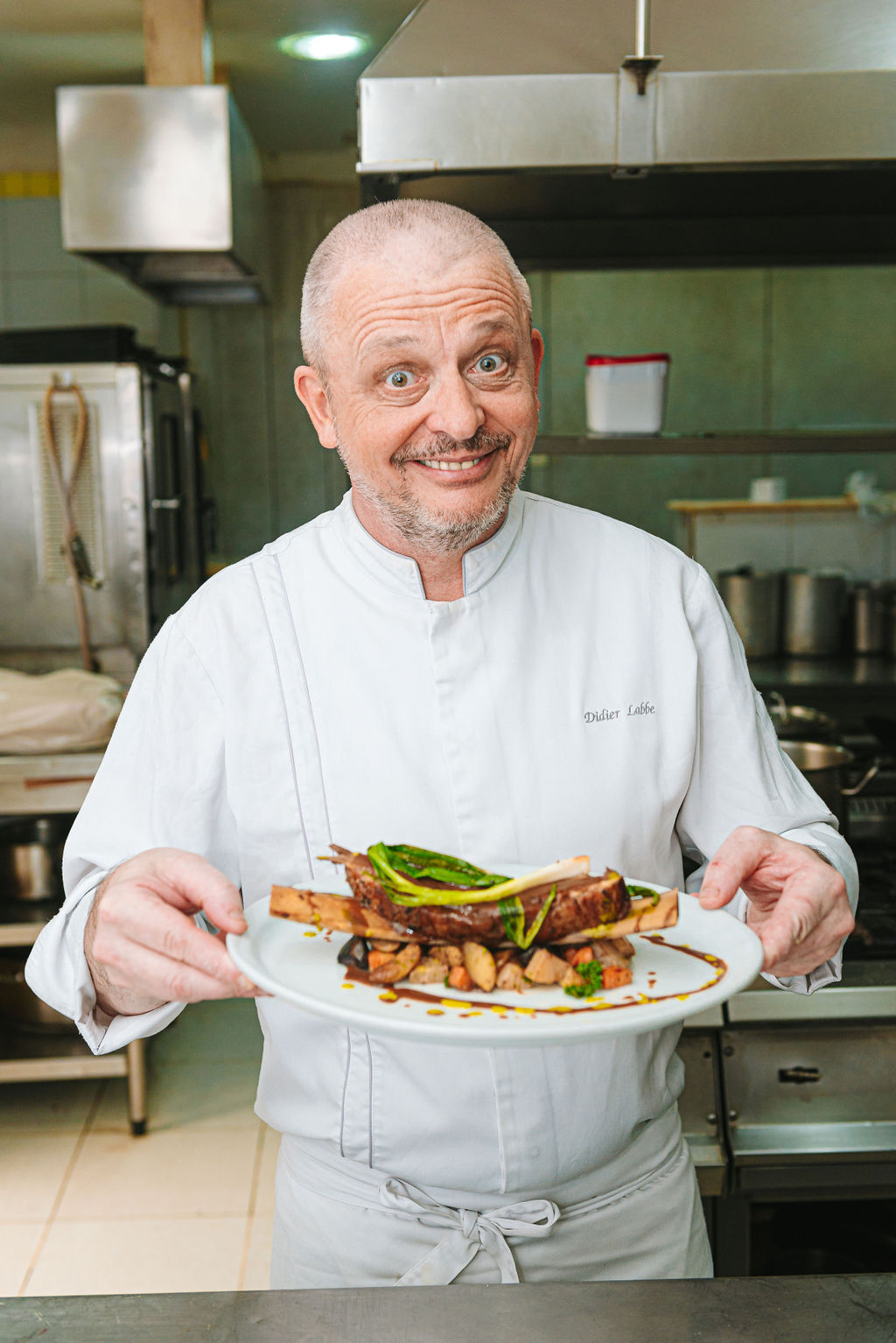 Foto mostra chef Didier com uniforme branco sorrindo mostrando prato de costela bovina