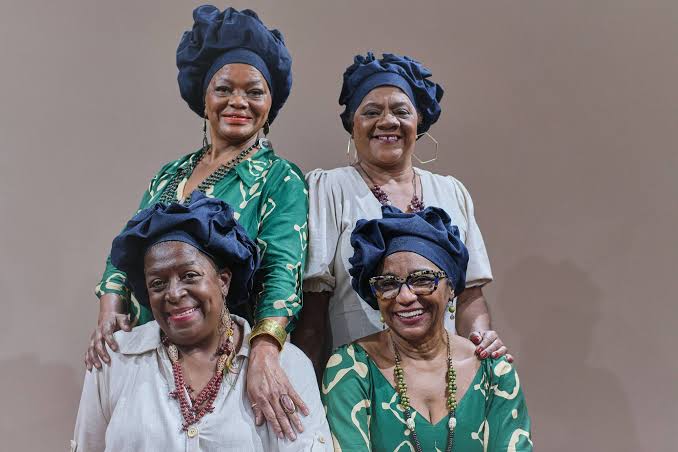 Foto mostra quatro mulheres negras idosas usando turbantes e sorrindo