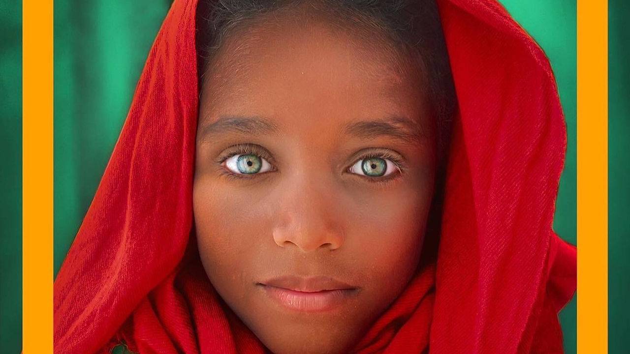 Foto mostra menino olhando para a câmera com olhos verdes, pele negra, usando um turbante vermelho. Acima está escrito "National Rio"