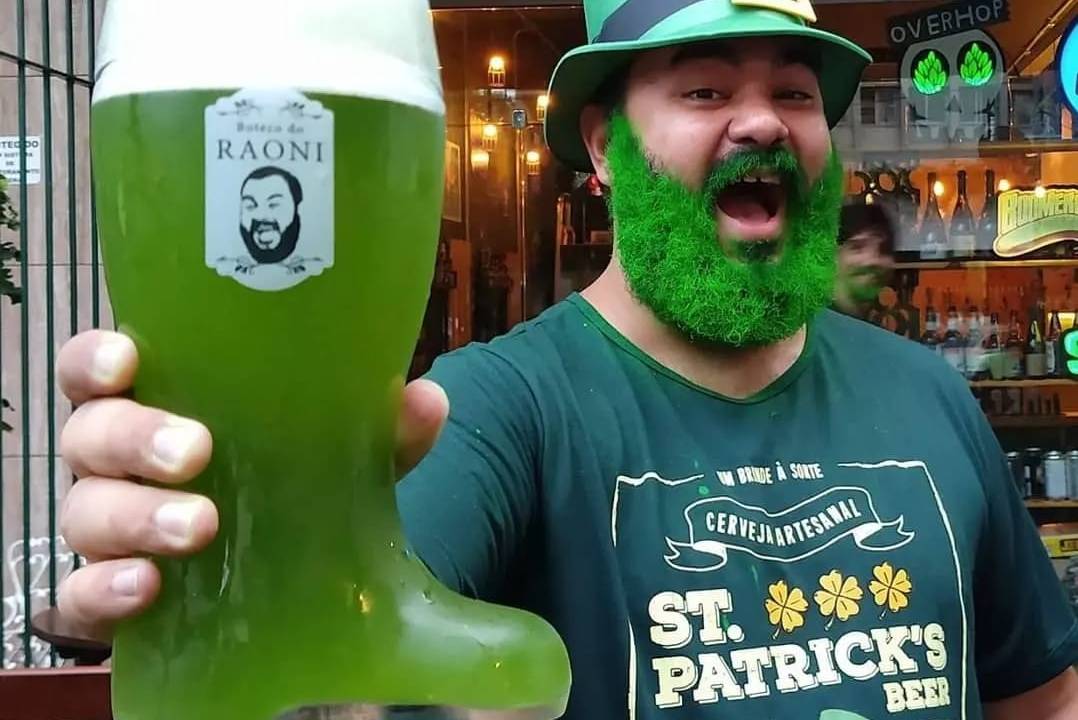 Foto mostra homem de barba verde com chope verde na mão sorrindo