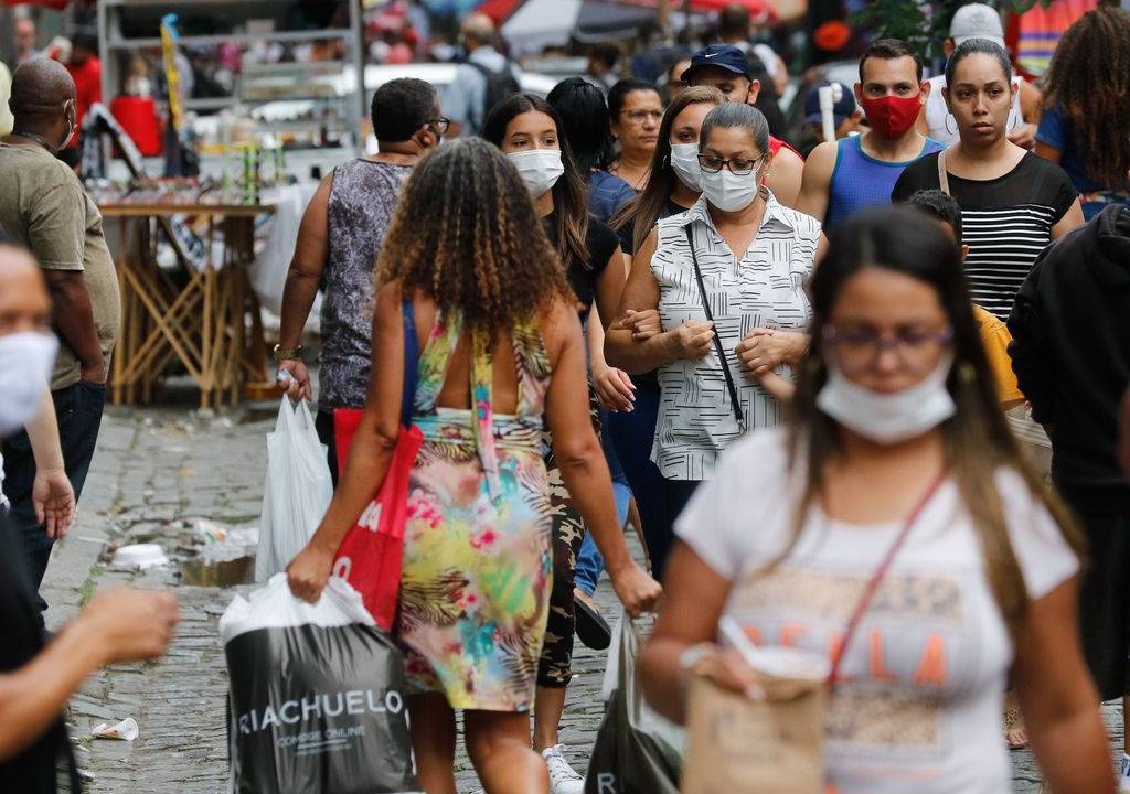Foto mostra pessoas usando máscaras contra a Covid-19 na rua. Uma mulher à frente usa a máscara abaixada