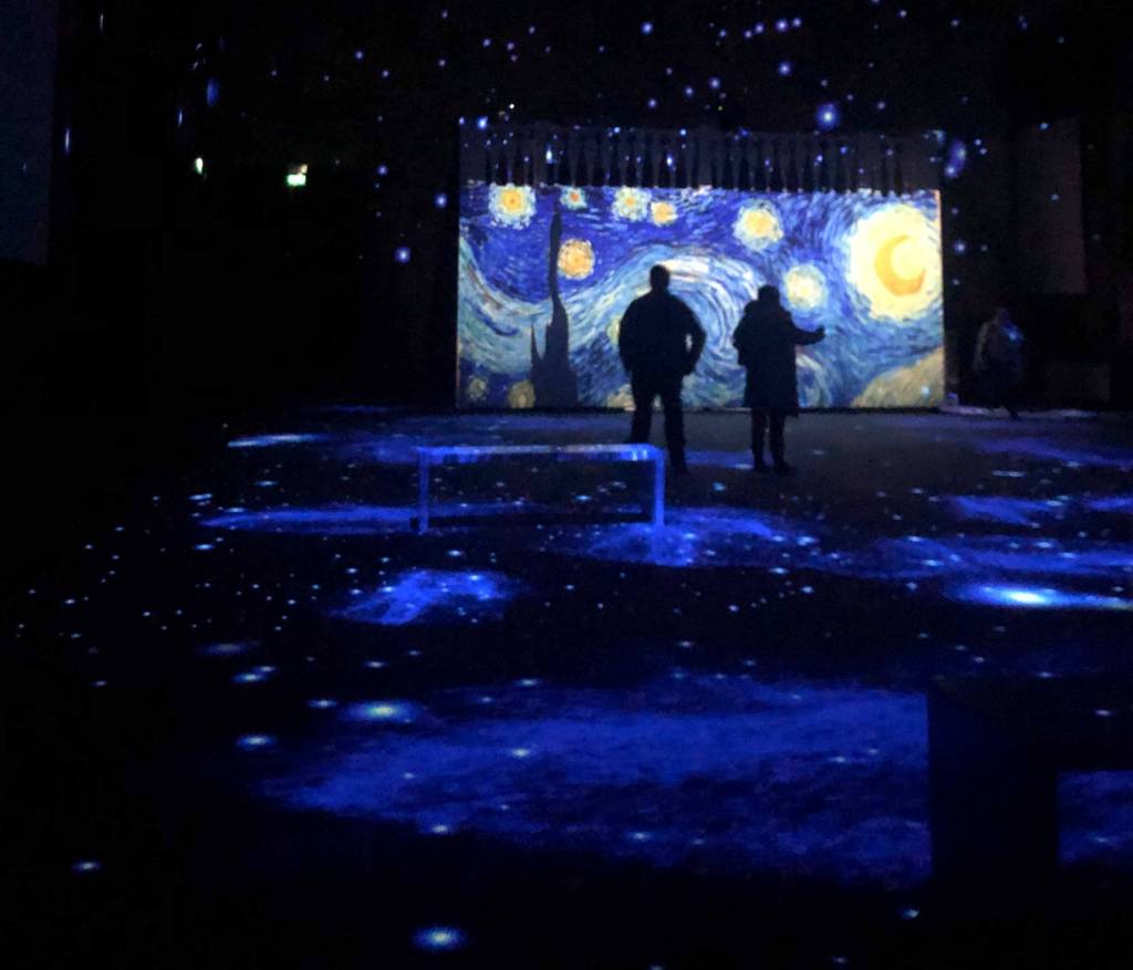 Parede tem projeção da tela A Noite Estrelada, de Van Gogh, e as sombras de duas pessoas que olham para a parede