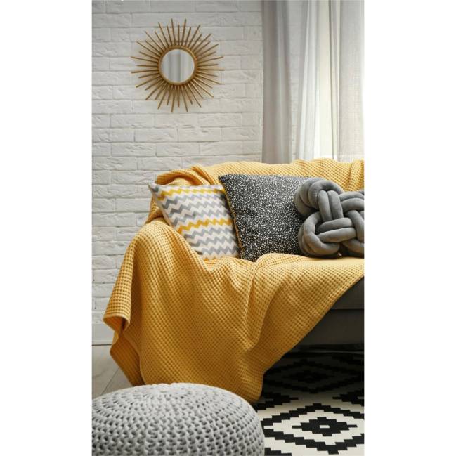 A imagem mostra um sofa com almofadas e manta amarela.