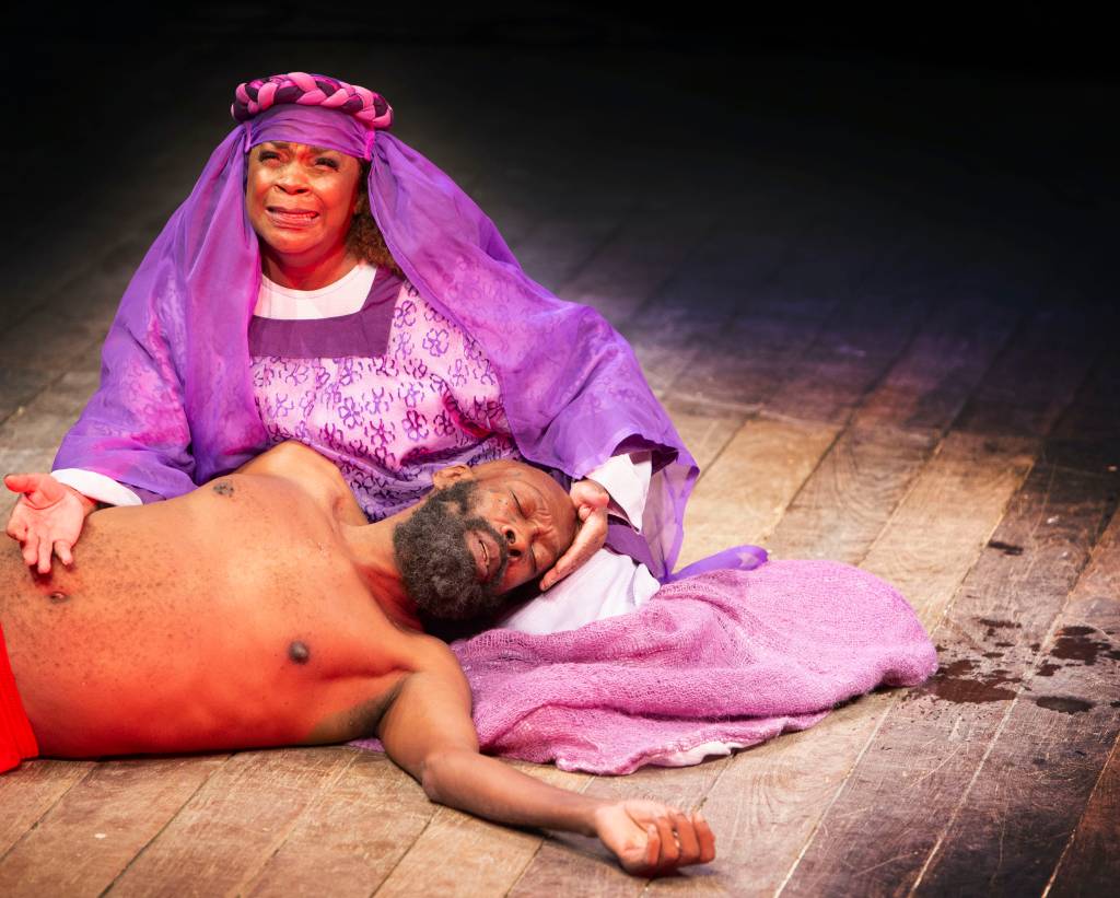A imagem traz Zezé Mota com véu roxo interpretando Maria segurando a cabeça de Thiago Justino, Jesus