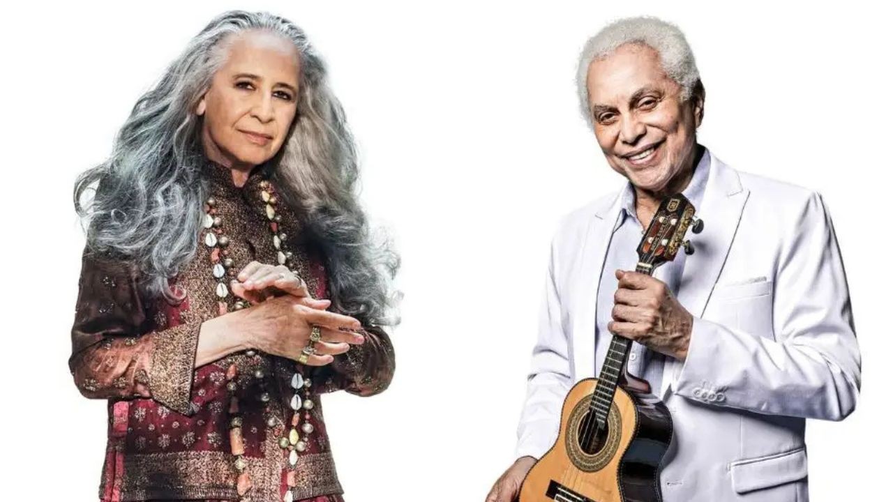 A cantora Gal Costa, com cabelos grisalhos longos e soltos, usa um casaco estampado e colares. Ao lado, o cantor e compositor João Bosco, sorridente, veste terno branco e segura um violão
