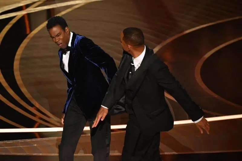 Frame do ator Will Smith dando um tapa no rosto do comediante Chris Rock.