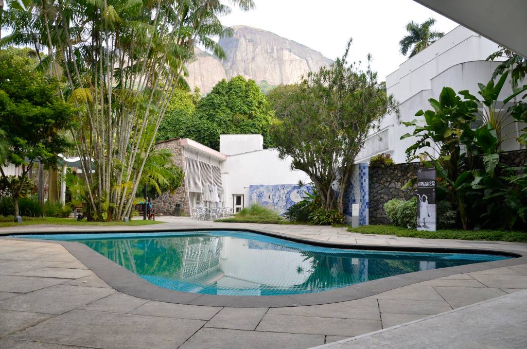 Ao fundo, a casa do Instituto Moreira Salles, cercada por vegetação. Em primeiro plano, a piscina do local.