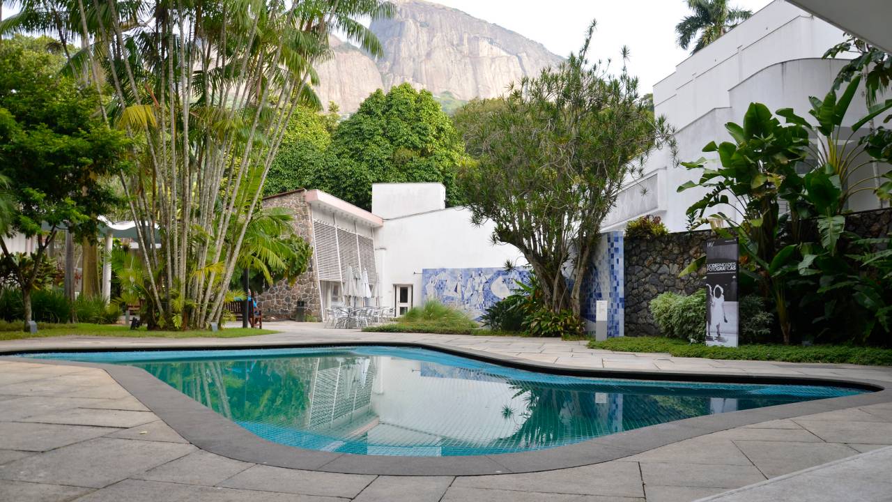 Ao fundo, a casa do Instituto Moreira Salles, cercada por vegetação. Em primeiro plano, a piscina do local.