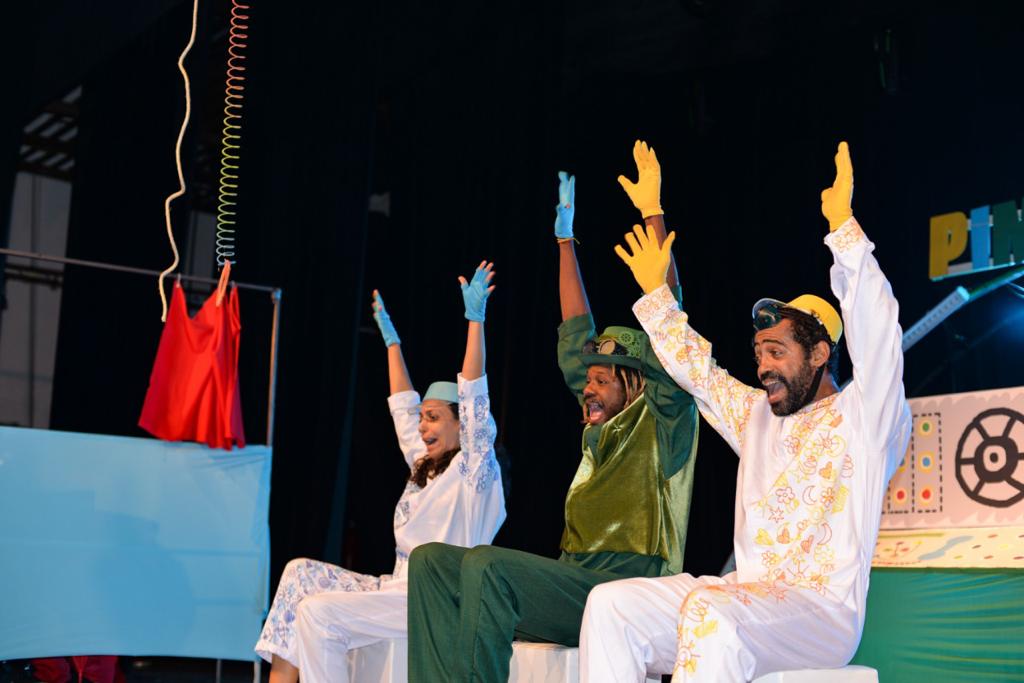 Foto mostra elenco da peça de Tarcísio Cisão. Dois atores e uma atriz estão com as mãos para o alto em cena e gritando