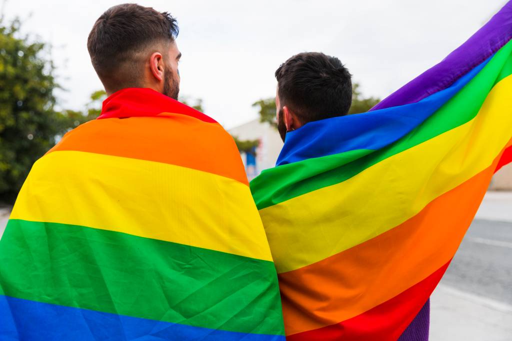 Foto mostra casal gay envolto em bandeiras do arco-íres
