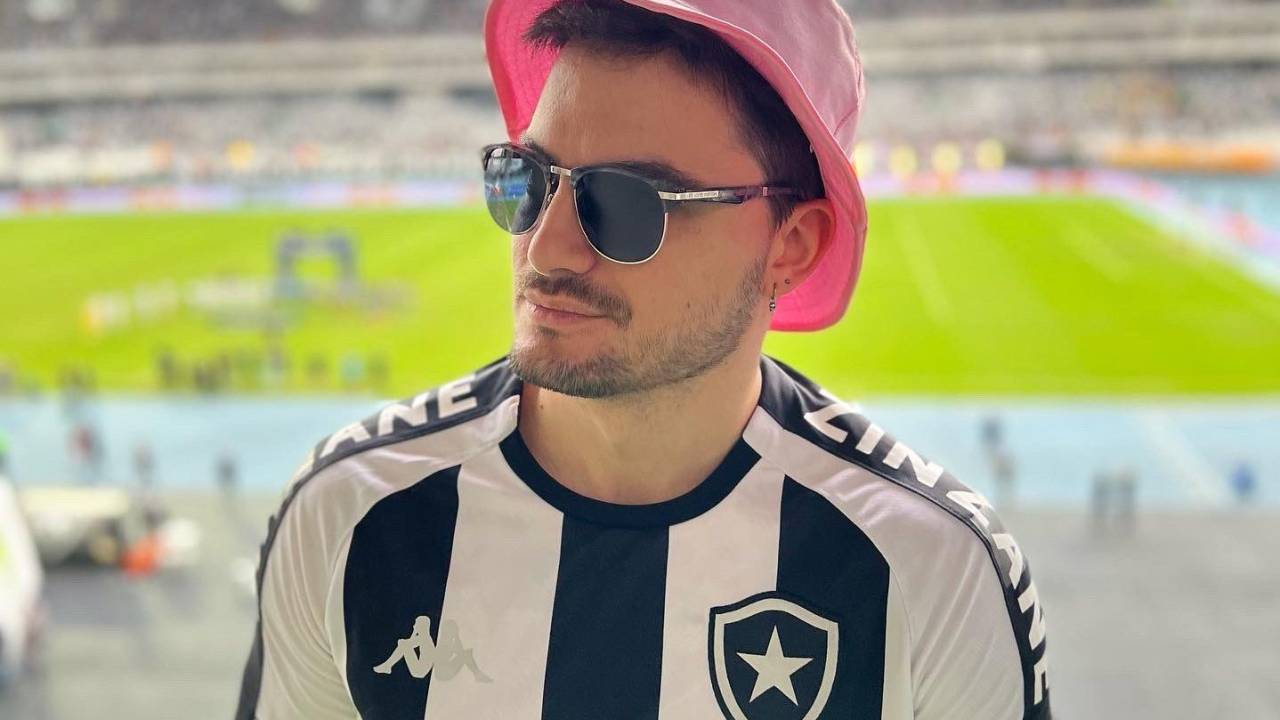 Felipe Neto usa camisa do Botafogo, chapéu rosa e óculos escuros. Ao fundo, o gramado do Engenhão.