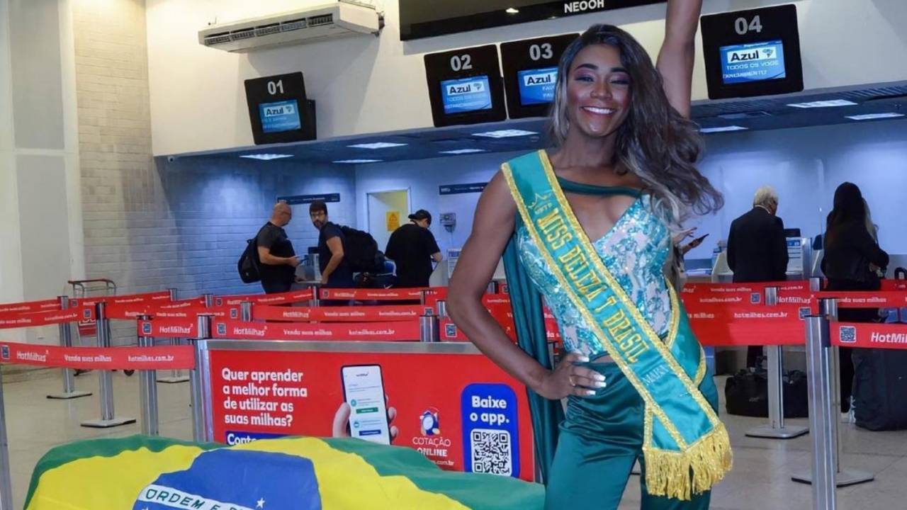 Foto mostra modelo trans em aeroporto usando uma faixa verde e amarela escrita "Miss T Brasil 2020"