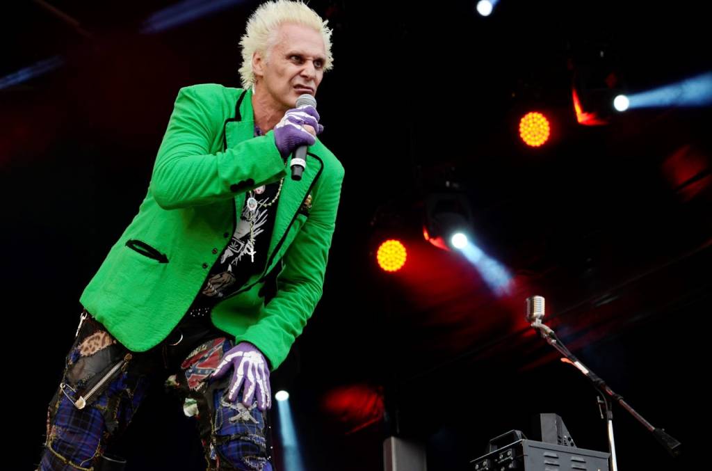 Foto mostra o cantor Supla se apresentando no palco e usando um blazer verde claro