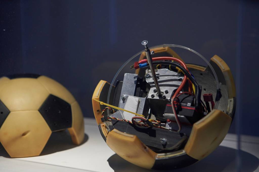 A obra consiste de metade de uma bola amarela e preta com aparelhos eletrônicos em seu interior.