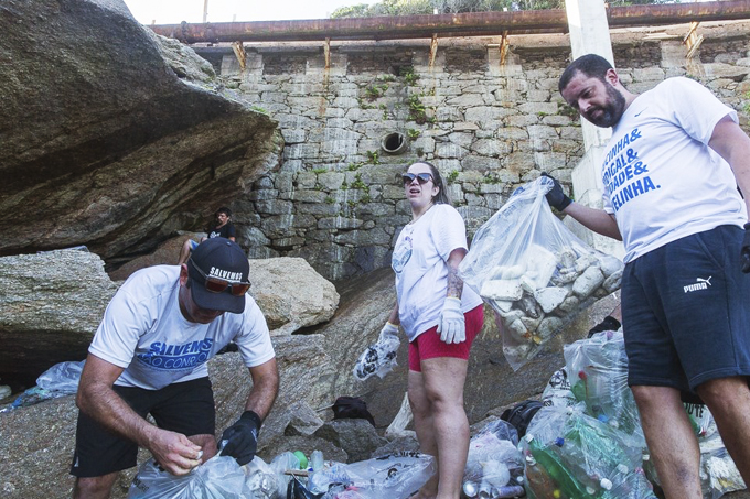 Foto mostra voluntários segurando sacolas de lixo