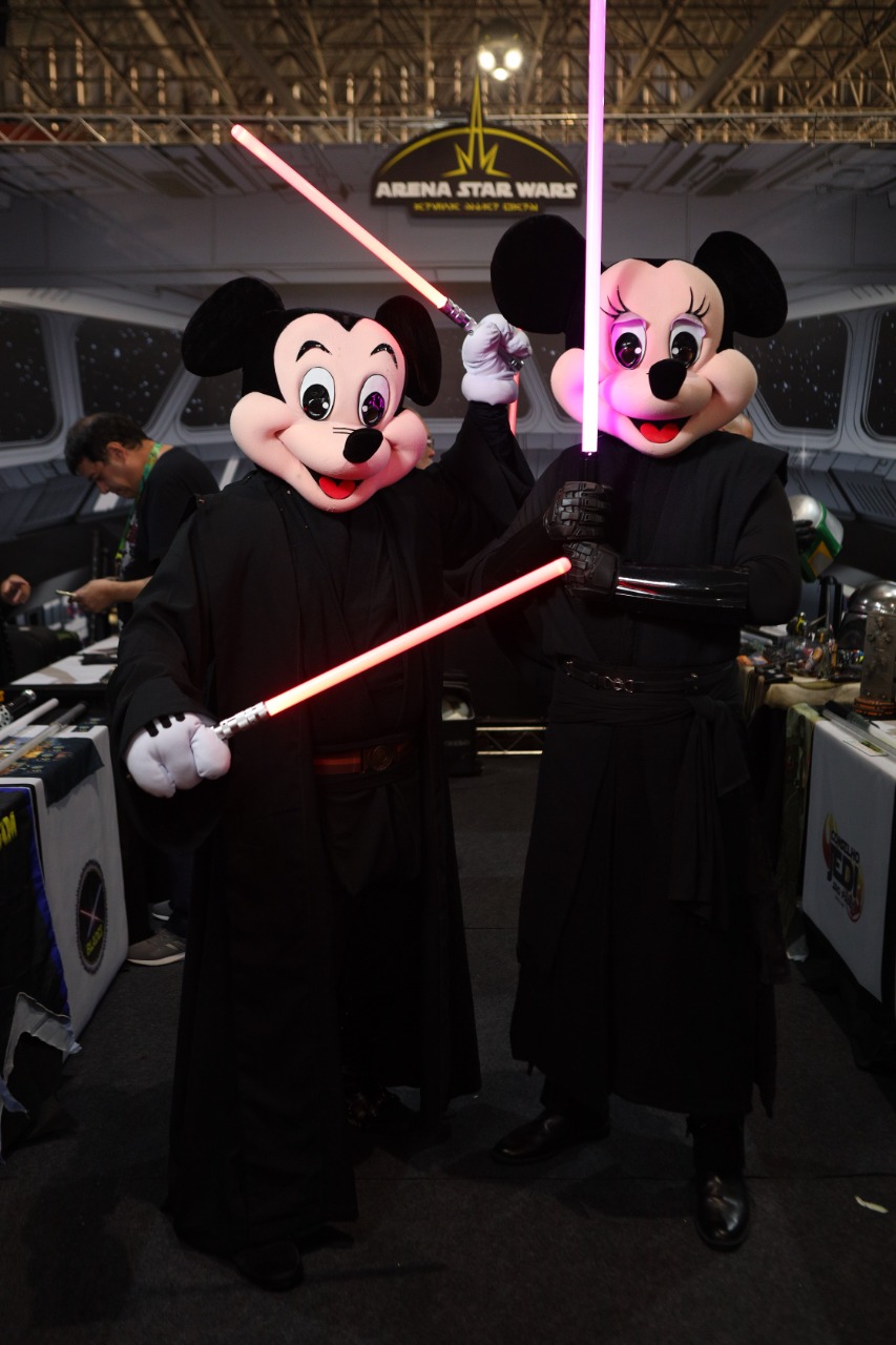 Foto mostra duas pessoas fantasiadas com cabeça de Mickey e roupa de Jedi de Star Wars