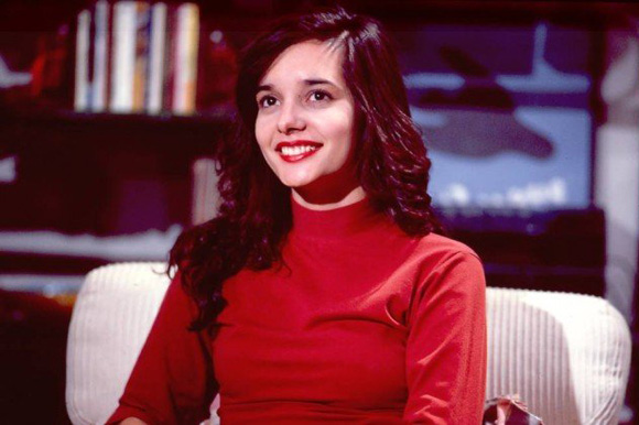 Foto da atriz Daniella Perez sorrindo e usando blusa vermelha de gola alta e manga comprida.