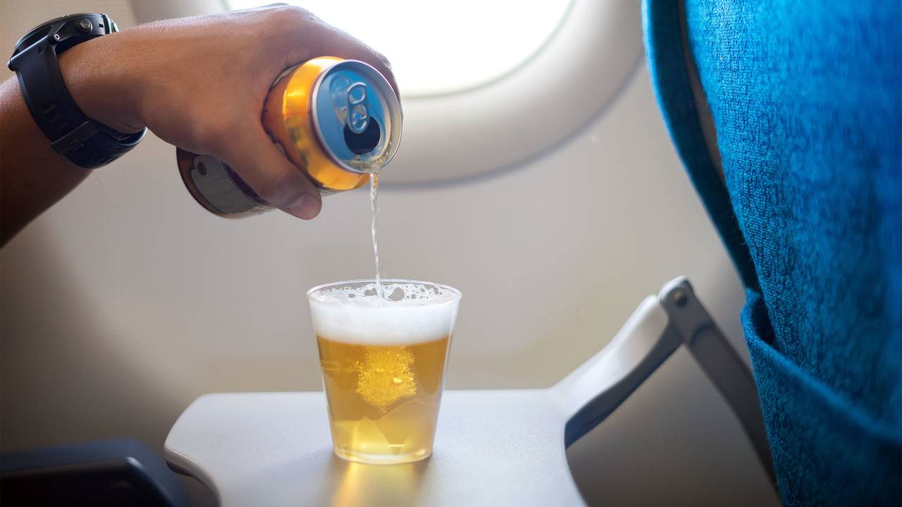 Foto mostra pessoa servindo cerveja em um copo dentro de um avião