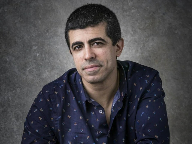 Marcius Melhem in a dark blue patterned jacket and shirt on a gray background