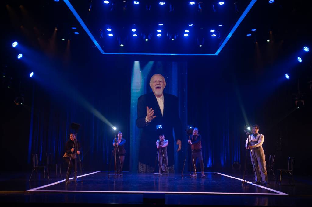 Os cinco atores no palco e, ao fundo, o telão com a imagem de Ney Latorraca.