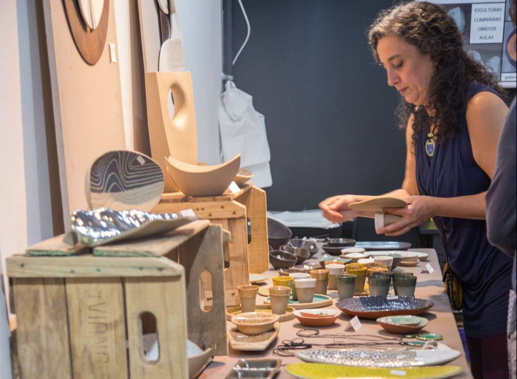Mulher olha produtos em mesa com cerâmicas.