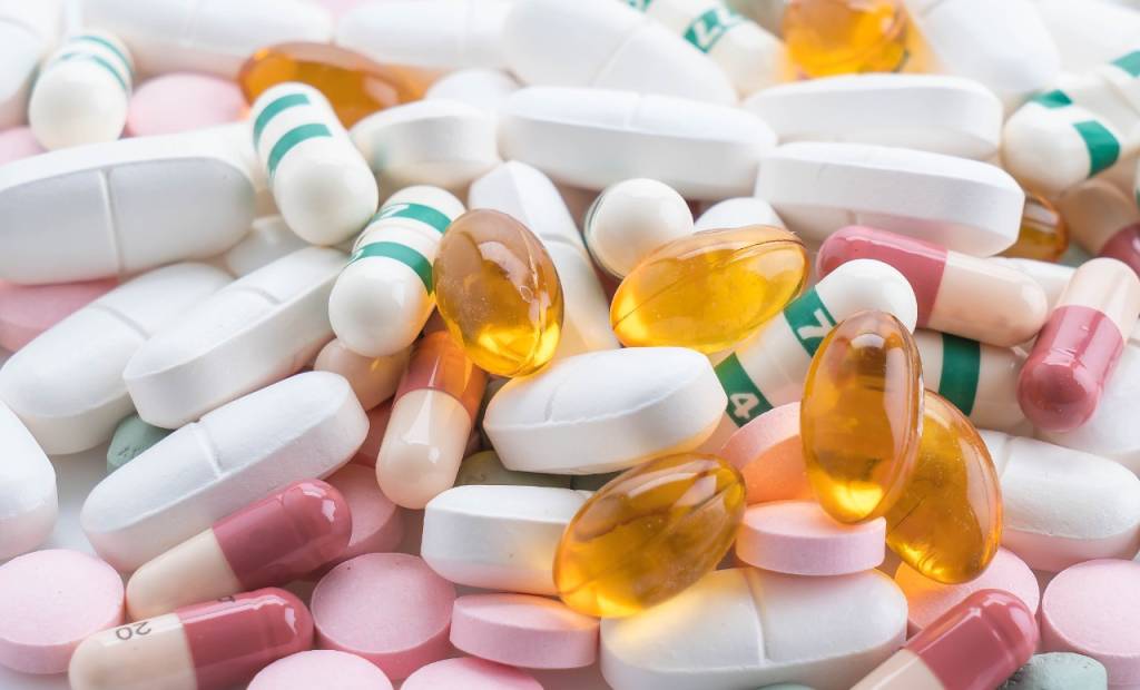 Imagem mostra comprimidos de remédios das cores branca, amarela, rosa e azul com verde