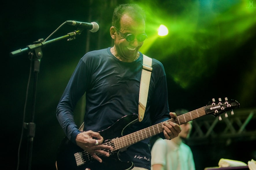 Jorge Ben Jor de blusa de manga comprida azul-marinho, tocando uma guitarra preta.