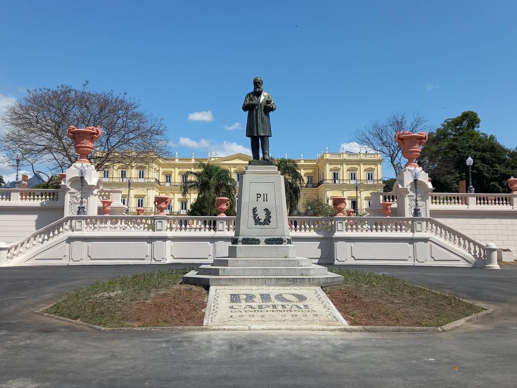 Foto mostra estátua em jardim em frente ao Museu Nacional