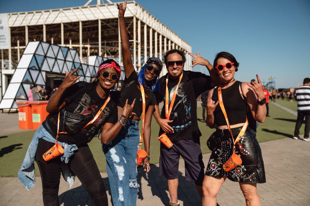 A foto mostra pessoas vestidas de preto segurando copo laranja do Itaú no gramado do Rock in Rio
