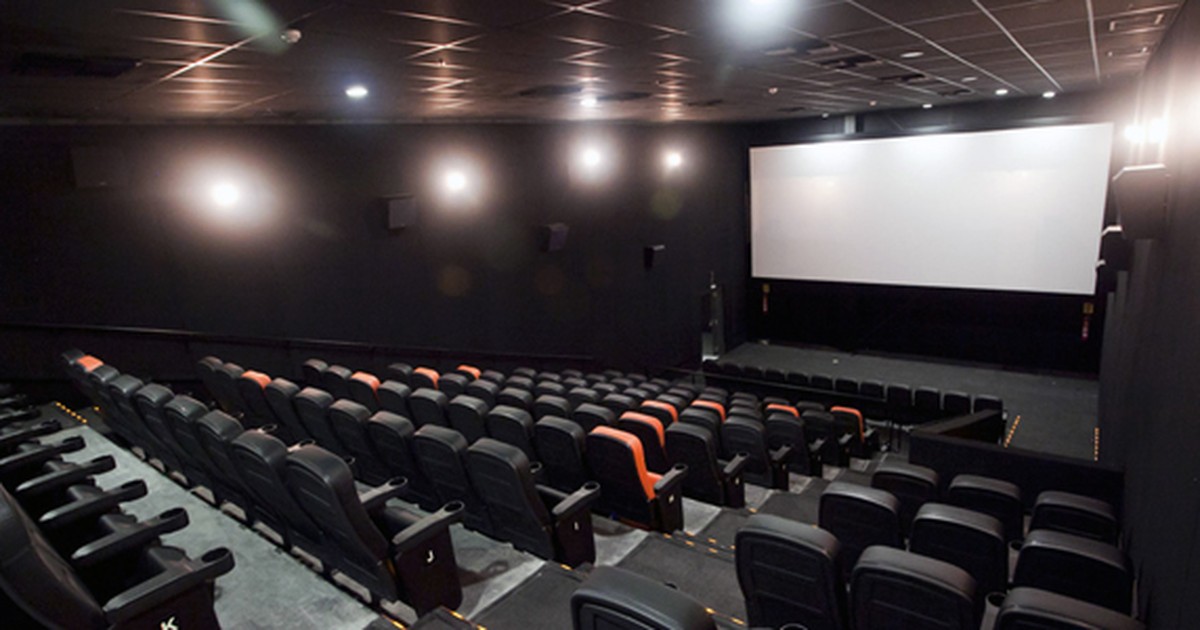 Sala de cinema com cadeiras pretas e a tela branca