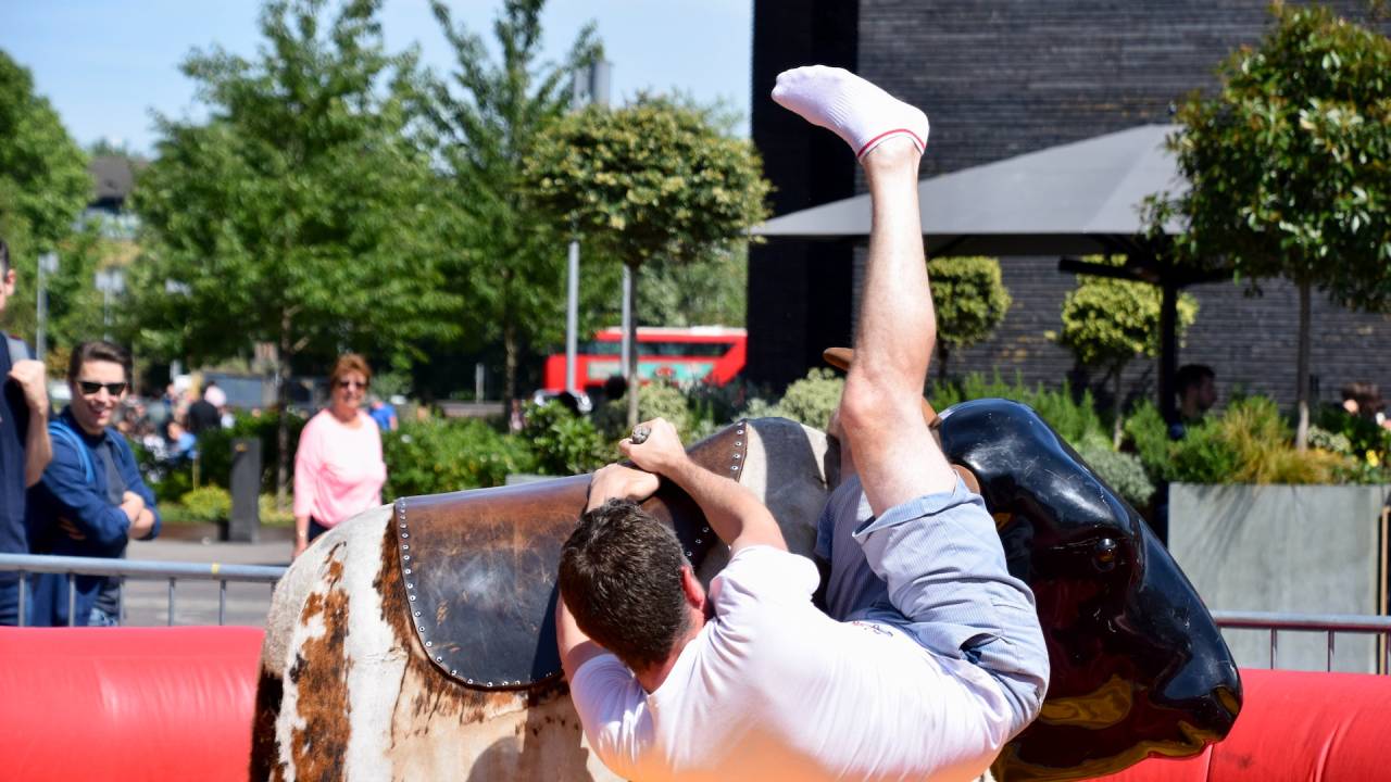 Foto de um homem branco de cabelos castanhos curtos caindo de um touro mecânico.