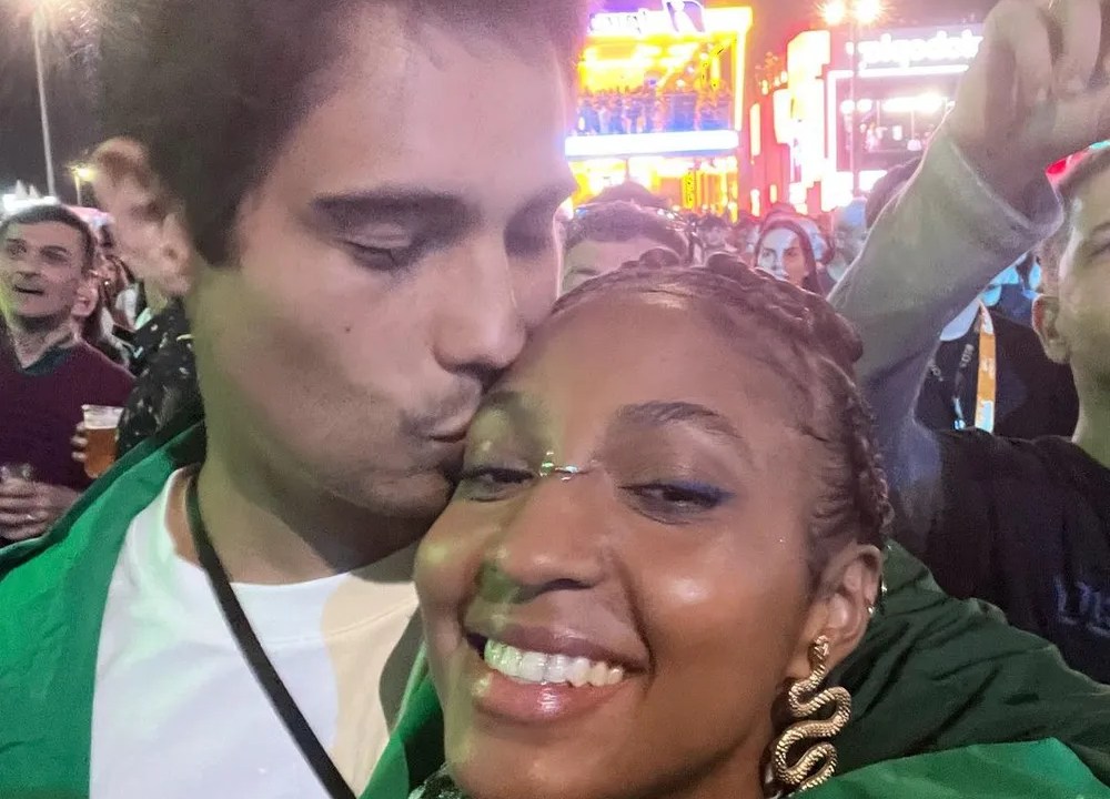 Foto de Domenica Dias e Danilo Mesquita abraçados durante um show no Rock in Rio. Ela sorri para a câmera e ele dá um beijo na testa dela