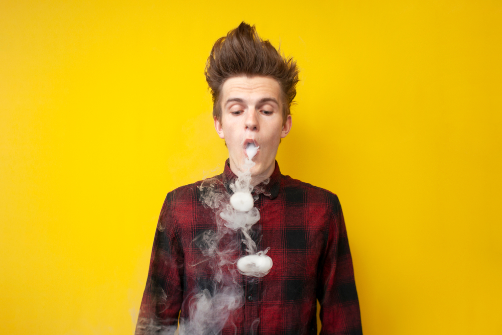Rapaz solta fumaça pela boca.