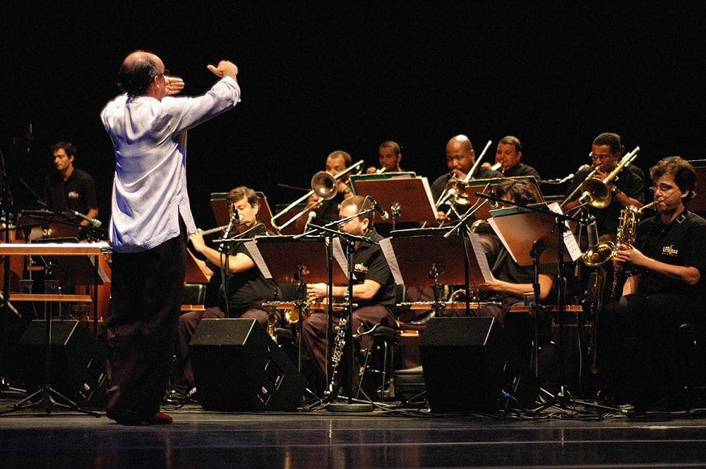 Foto mostra orquestra se apresentando com maestro à frente