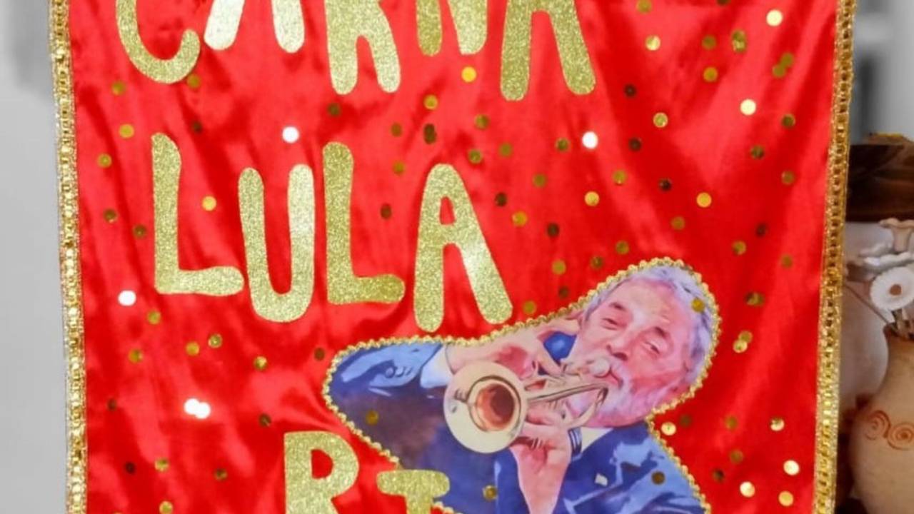Foto mostra bandeira carvanalesca vermelha escrita CarnaLula RJ e com uma imagem do Lula tocando um trompete