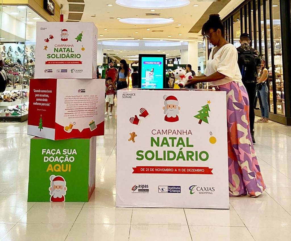 Foto mostra moça colocando doação em uma caixa escrita "Natal Solidário"