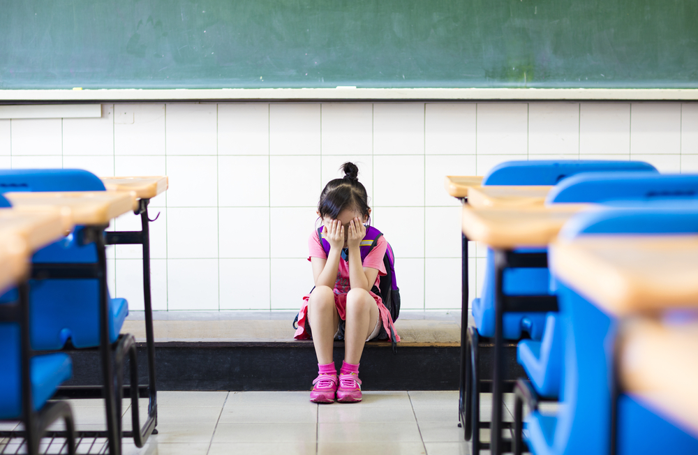 Aluna leva as mãos ao rosto em sala de aula vazia.