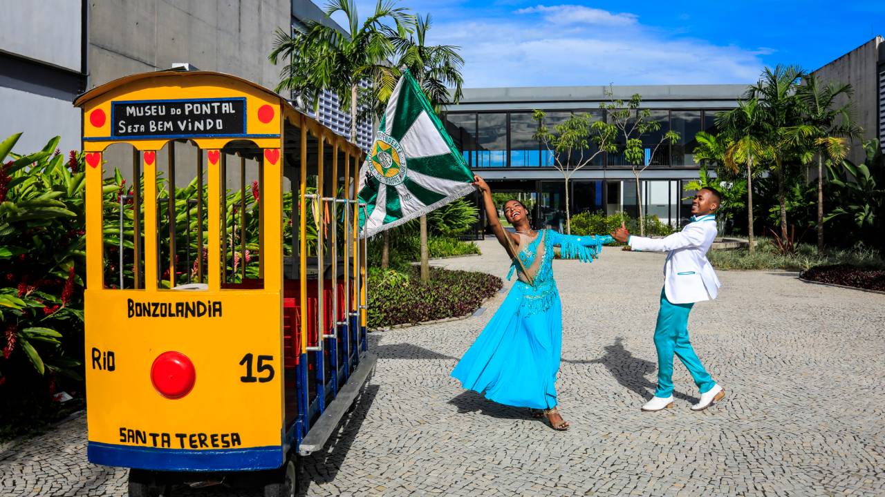 Foto mostra porta-bandeira e mestre-sala da Mocidade dançando em frente ao Museu do Pontal
