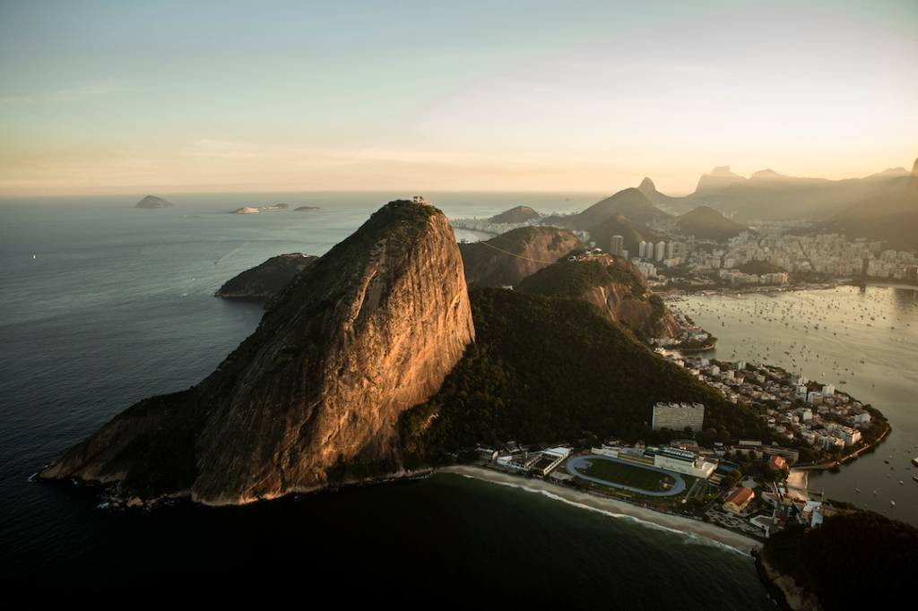 Foto aérea mostra Pão de Açúcar ao pôr do sol. É possível ver também na foto o bairro da Urca, a enseada e Botafogo e parte da Zona Sul do Rio