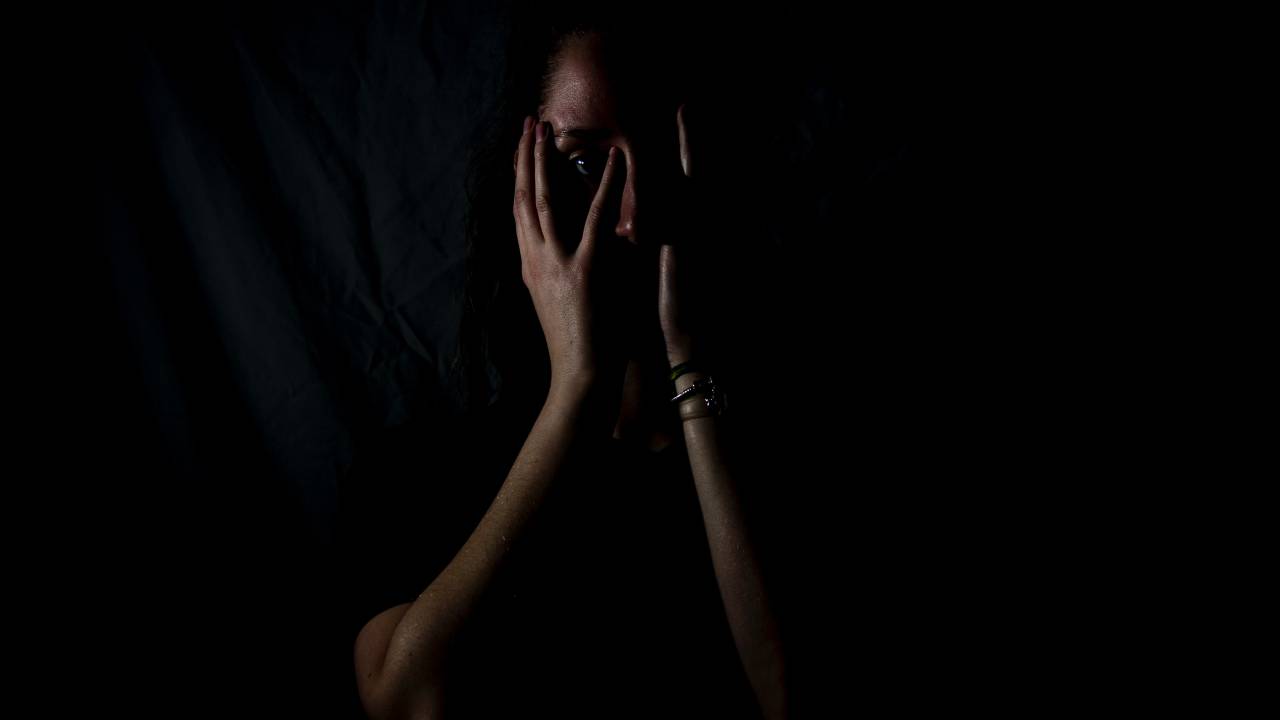 Foto mostra mulher no escuro com cara de medo