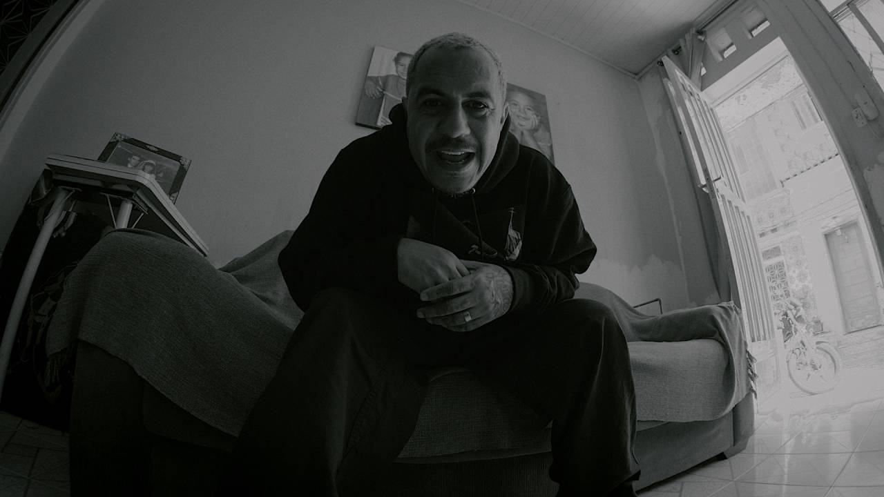 Marcelo D2 sentado na cama e cantando em foto em preto e branco