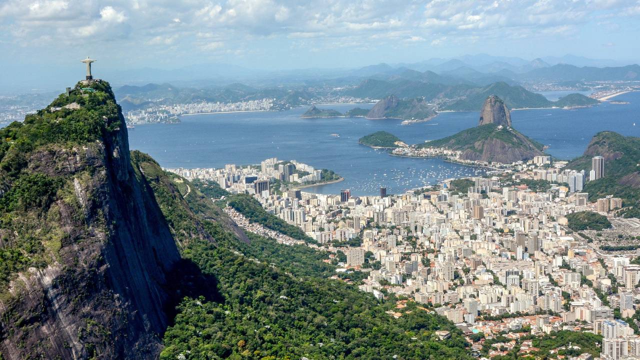 Foto mostra paisagem do Rio com o Morro do Corcovado em primeiro plano e o Pão de Açúcar e a Baía de Guanabara ao fundo