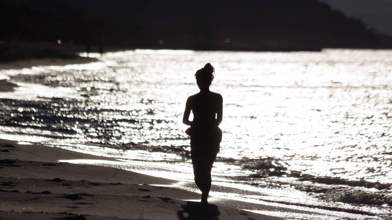 Mulher andando reflexiva à beira do mar