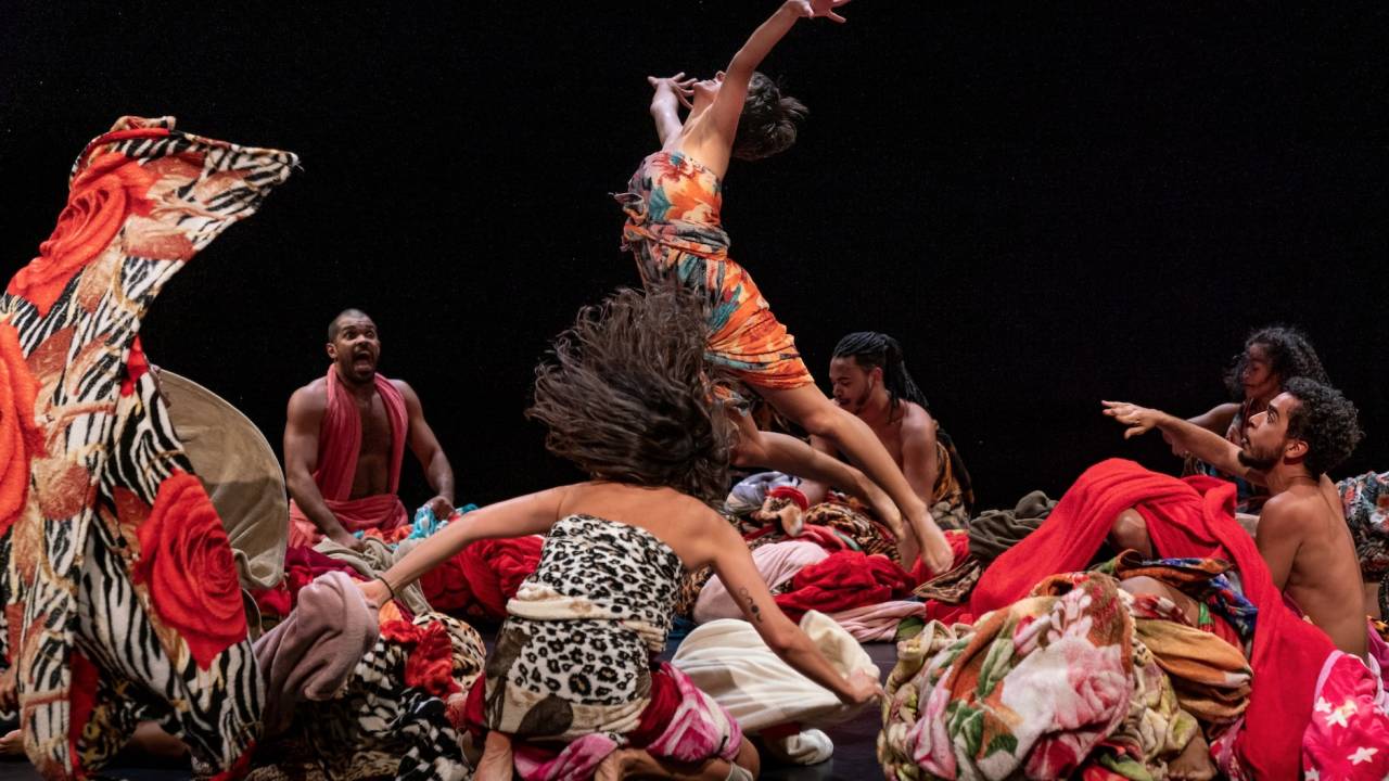 Cena do espetáculo de dança Encantado, de Lia Rodrigues, com pessoas no chão em círculo e uma mulher pulando para o alto.