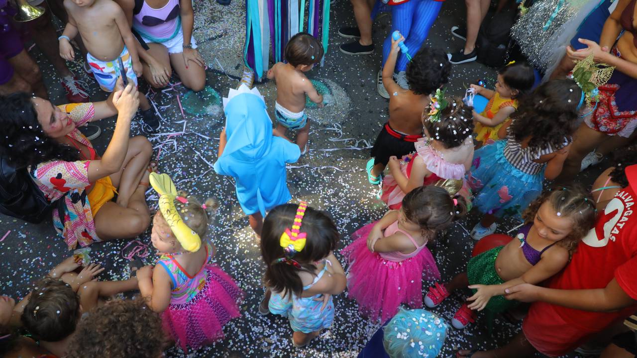 Foto tirada de cima de crianças fantasiadas no Carnaval, com o chão cheio de confete.