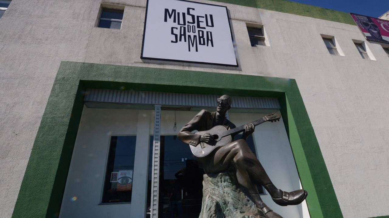A fachada do Museu do Samba, com uma placa com o nome e, em primeiro plano, uma estátua do sambista Cartola tocando violão.