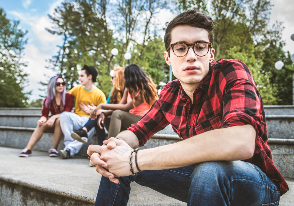 Jovem sentado numa escada, distante de um grupo.