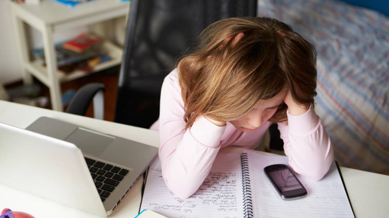 Criança leva as mãos à cabeça em gesto de desespero diante do computador e do celular.